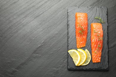 Photo of Seafood. Pieces of salmon fillet, thyme and lemon slices on black textured table, top view. Space for text