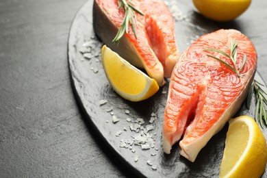 Photo of Seafood. Salmon steaks, spices and lemon wedges on black textured table, closeup
