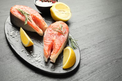 Photo of Seafood. Salmon steaks, spices and lemon wedges on black textured table, closeup. Space for text