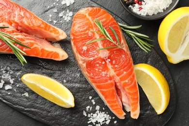 Photo of Seafood. Salmon steaks, spices and lemon on black table, flat lay