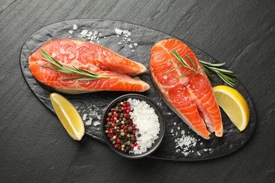 Photo of Seafood. Salmon steaks, spices and lemon wedges on black textured table, top view