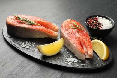 Photo of Seafood. Salmon steaks, spices and lemon wedges on black textured table, closeup