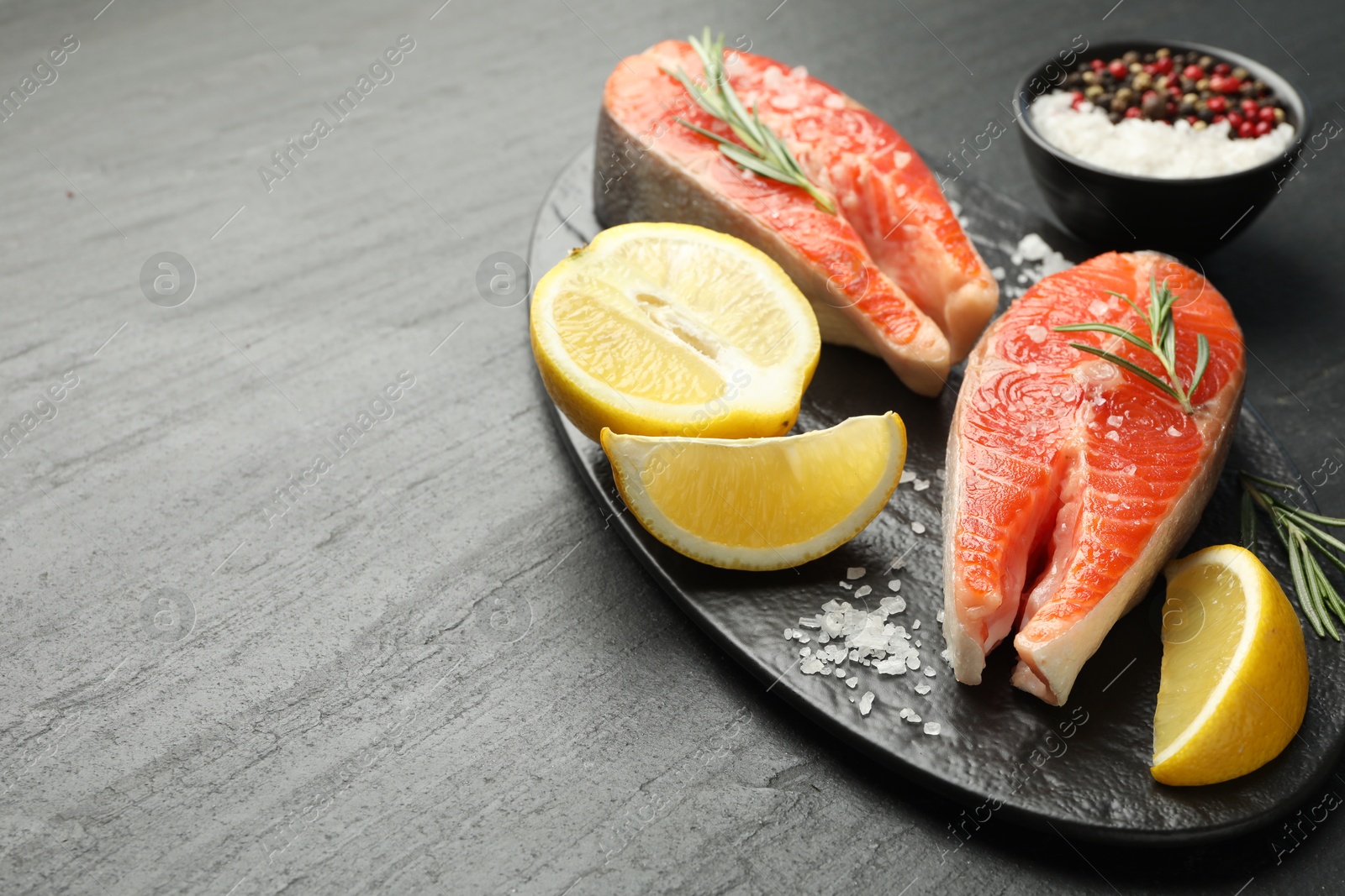 Seafood. Salmon steaks, spices and lemon on black textured table, closeup. Space for text Photo of Seafood. Salmon steaks, spices and lemon on black textured table, closeup. Space for text