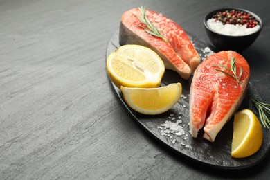 Photo of Seafood. Salmon steaks, spices and lemon on black textured table, closeup. Space for text