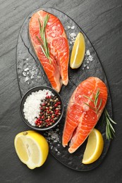 Photo of Seafood. Salmon steaks, spices and lemon on black textured table, top view