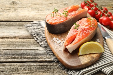 Photo of Seafood. Salmon steaks, spices, lemon wedge and tomatoes on wooden table, closeup. Space for text