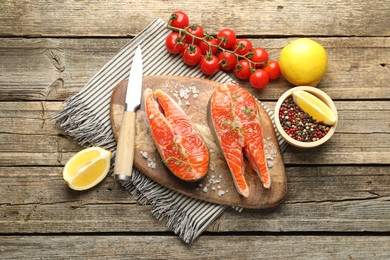 Photo of Seafood. Salmon steaks, spices, tomatoes, lemons and knife on wooden table, flat lay