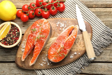 Photo of Seafood. Salmon steaks, spices, tomatoes, lemons and knife on wooden table, flat lay