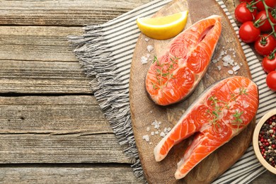 Photo of Seafood. Salmon steaks, spices, tomatoes and lemon wedge on wooden table, flat lay. Space for text