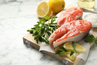 Photo of Seafood. Fresh raw salmon steaks, parsley and lemons on white marble table, closeup