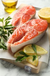 Photo of Seafood. Fresh raw salmon steaks, parsley and pieces of lemon on white marble table, closeup
