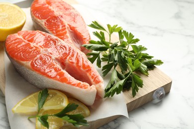 Photo of Seafood. Fresh raw salmon steaks, parsley and pieces of lemon on white marble table, closeup