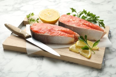 Photo of Seafood. Fresh raw salmon steaks, parsley, pieces of lemon and knife on white marble table, closeup
