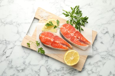 Photo of Seafood. Fresh raw salmon steaks, parsley, pieces of lemon and salt on white marble table, top view
