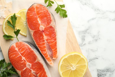 Photo of Seafood. Fresh raw salmon steaks, parsley and pieces of lemon on white marble table, top view. Space for text
