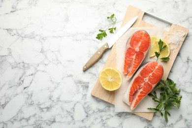 Photo of Seafood. Fresh raw salmon steaks, parsley, pieces of lemon and salt on white marble table, top view. Space for text