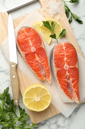 Photo of Seafood. Fresh raw salmon steaks, parsley, pieces of lemon and salt on white marble table, flat lay