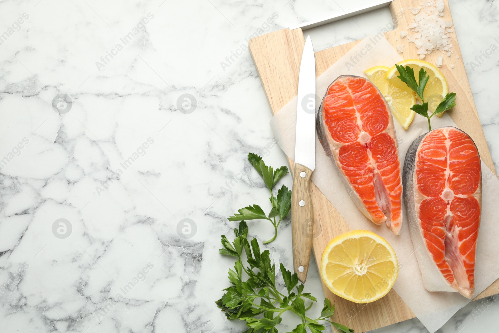 Seafood. Fresh raw salmon steaks, parsley, pieces of lemon and knife on white marble table, flat lay. Space for text Photo of Seafood. Fresh raw salmon steaks, parsley, pieces of lemon and knife on white marble table, flat lay. Space for text