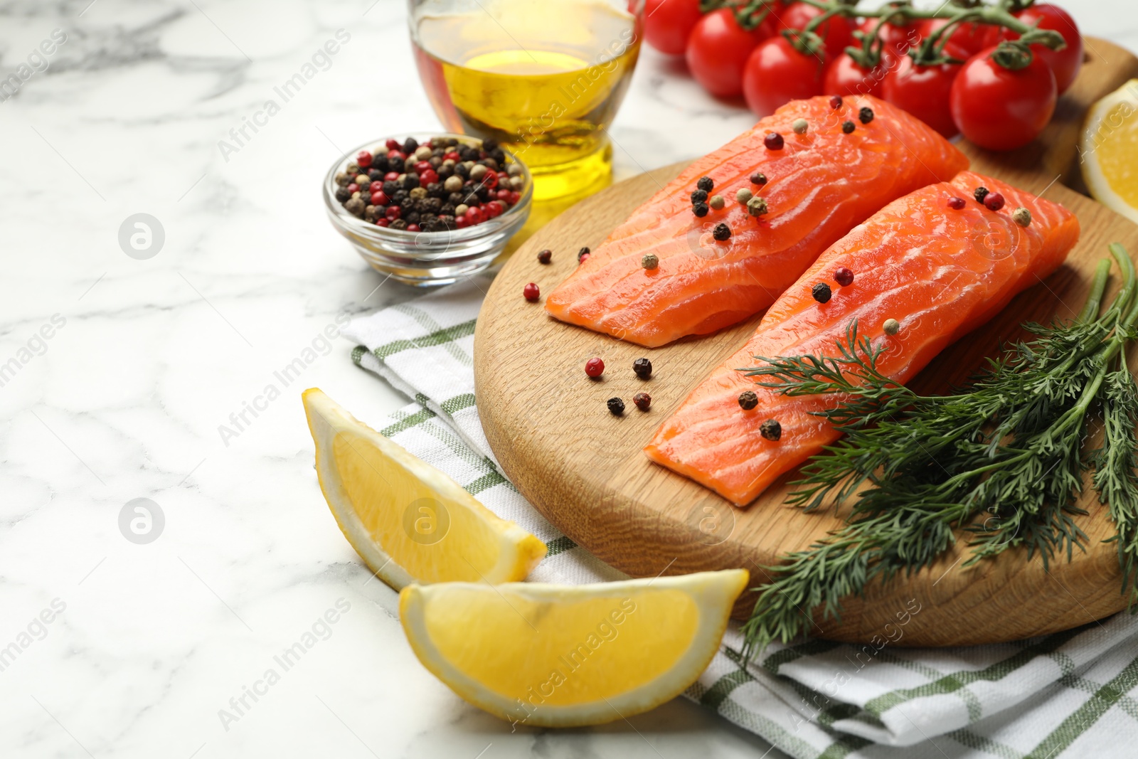 Seafood. Pieces of salmon fillet, tomatoes, oil, spices and lemon wedges on white marble table, closeup Photo of Seafood. Pieces of salmon fillet, tomatoes, oil, spices and lemon wedges on white marble table, closeup