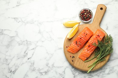 Photo of Seafood. Pieces of salmon fillet, spices and lemon wedges on white marble table, flat lay. Space for text