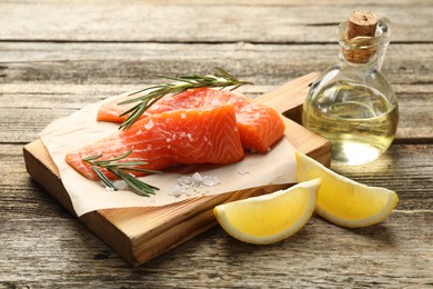 Photo of Seafood. Pieces of salmon fillet, spices, oil and lemon wedges on wooden table, closeup