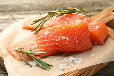 Photo of Seafood. Pieces of salmon fillet, rosemary and salt on table, closeup