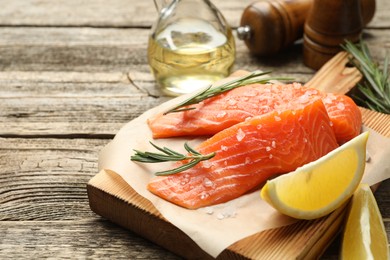 Photo of Seafood. Pieces of salmon fillet, spices, oil and lemon wedges on wooden table, closeup