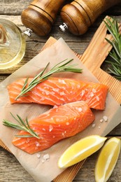 Photo of Seafood. Pieces of salmon fillet, spices, oil and lemon wedges on wooden table, flat lay