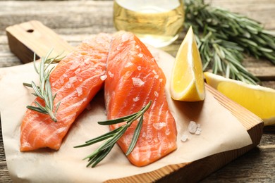 Photo of Seafood. Pieces of salmon fillet, spices, oil and lemon wedges on wooden table, closeup