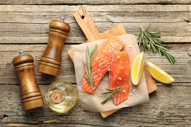 Photo of Seafood. Pieces of salmon fillet, spices, oil and lemon wedges on wooden table, flat lay