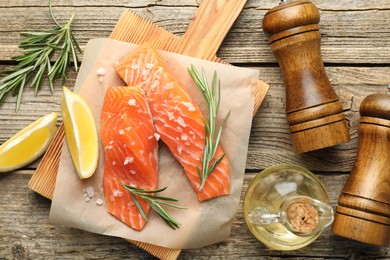Photo of Seafood. Pieces of salmon fillet, spices, oil and lemon wedges on wooden table, flat lay