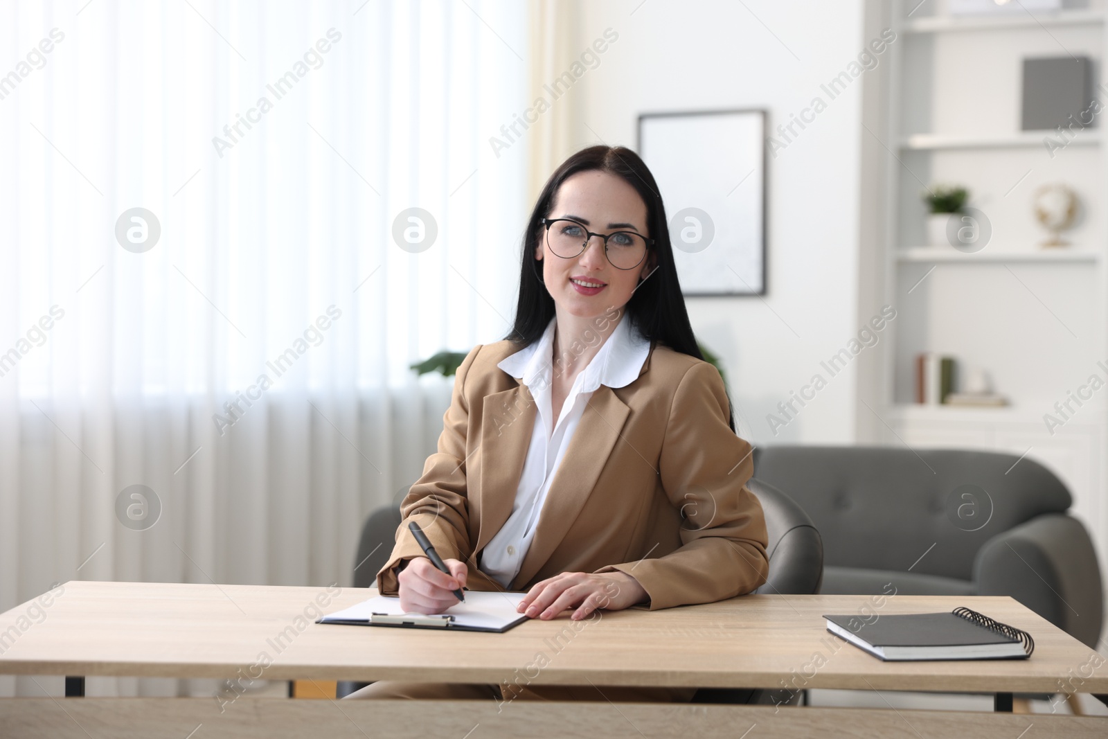 Professional psychologist with clipboard and pen at table in office Photo of Professional psychologist with clipboard and pen at table in office