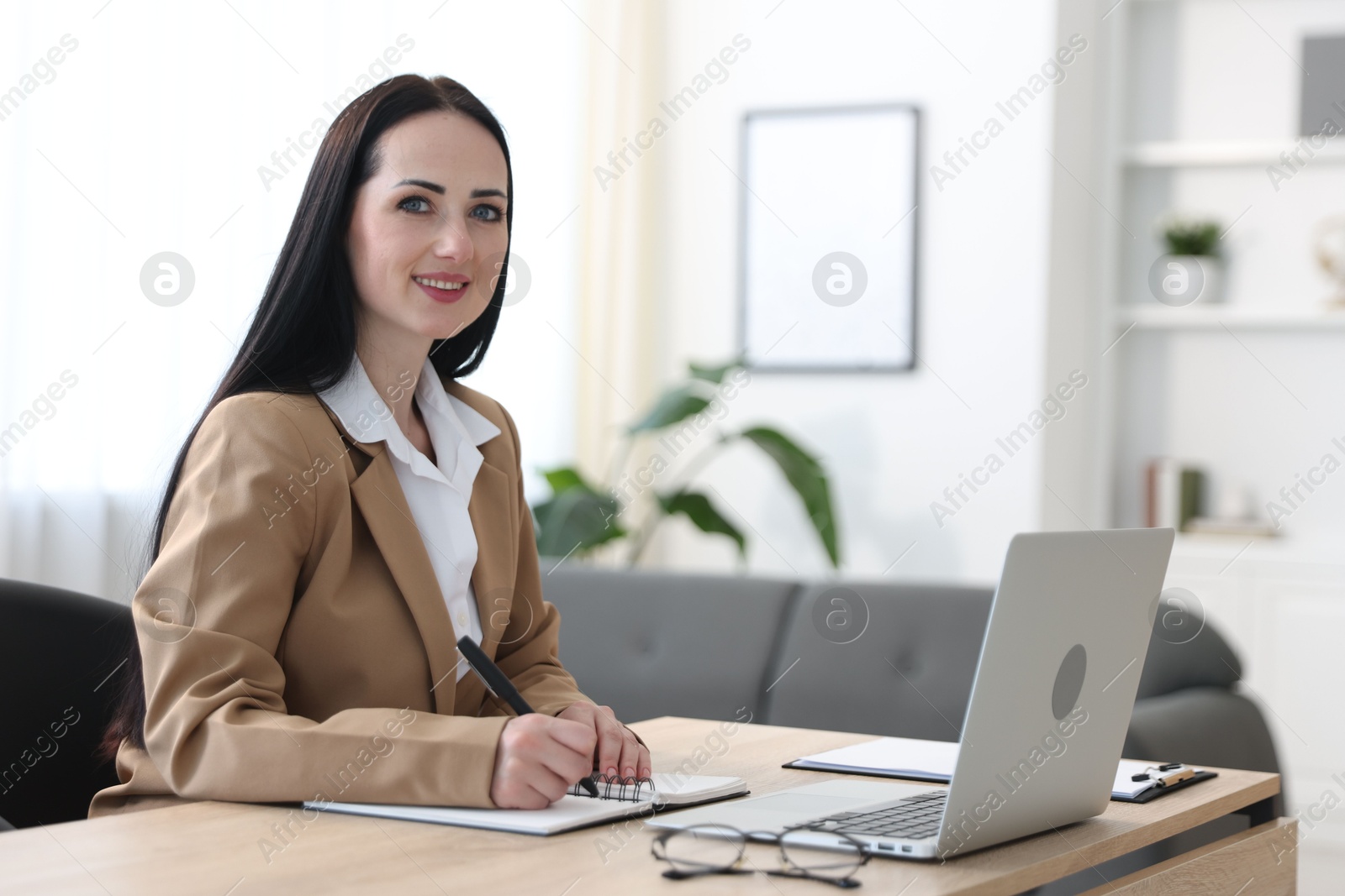 Professional psychologist taking notes while working with laptop at table in office Photo of Professional psychologist taking notes while working with laptop at table in office