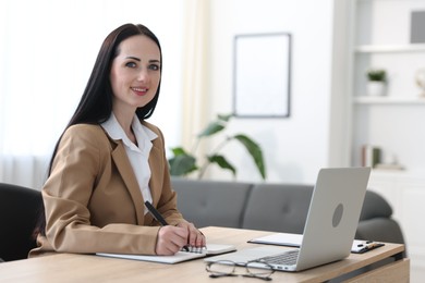 Photo of Professional psychologist taking notes while working with laptop at table in office