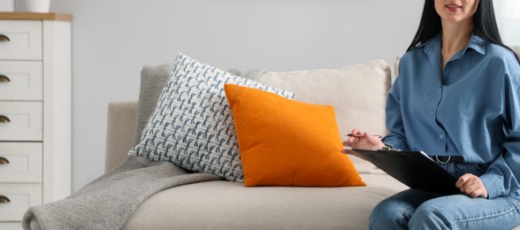 Photo of Professional psychologist with clipboard and pen on sofa in office, closeup