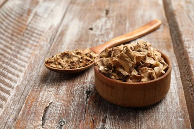 Photo of Pieces of dry chicory roots in bowl and spoon on wooden table, closeup