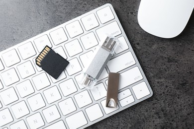 Photo of SD memory card, USB flash drives, keyboard and mouse on dark grey table, flat lay