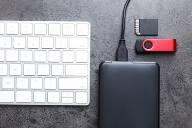 Photo of SD memory card, USB flash drive, hard disk drive with cable and keyboard on dark grey table, flat lay