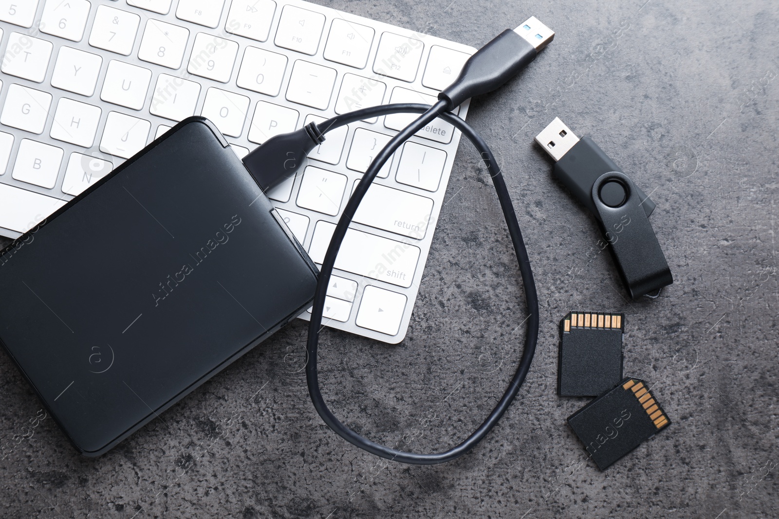 SD memory cards, USB flash drive, hard disk drive with cable and keyboard on dark grey table, flat lay Photo of SD memory cards, USB flash drive, hard disk drive with cable and keyboard on dark grey table, flat lay