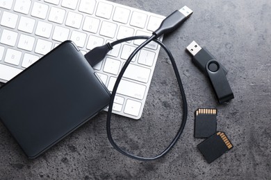 Photo of SD memory cards, USB flash drive, hard disk drive with cable and keyboard on dark grey table, flat lay
