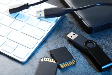 Photo of SD memory cards, USB flash drive, hard disk drive with cable and keyboard on dark grey table, closeup