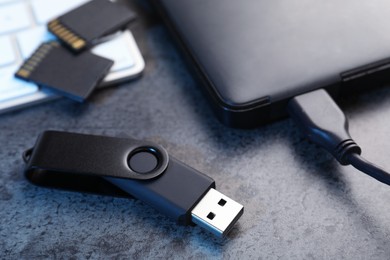 Photo of SD memory cards, USB flash drive, hard disk drive with cable and keyboard on dark grey table, closeup