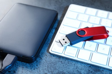 Photo of USB flash drive, hard disk drive and keyboard on dark grey table, closeup