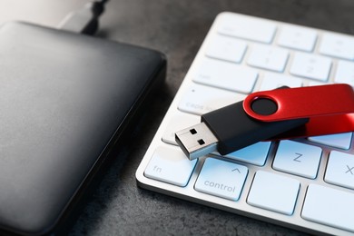 Photo of USB flash drive, hard disk drive and keyboard on dark grey table, closeup