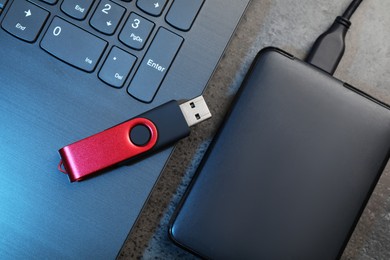 Photo of USB flash drive, hard disk drive with cable and laptop on dark grey table, flat lay