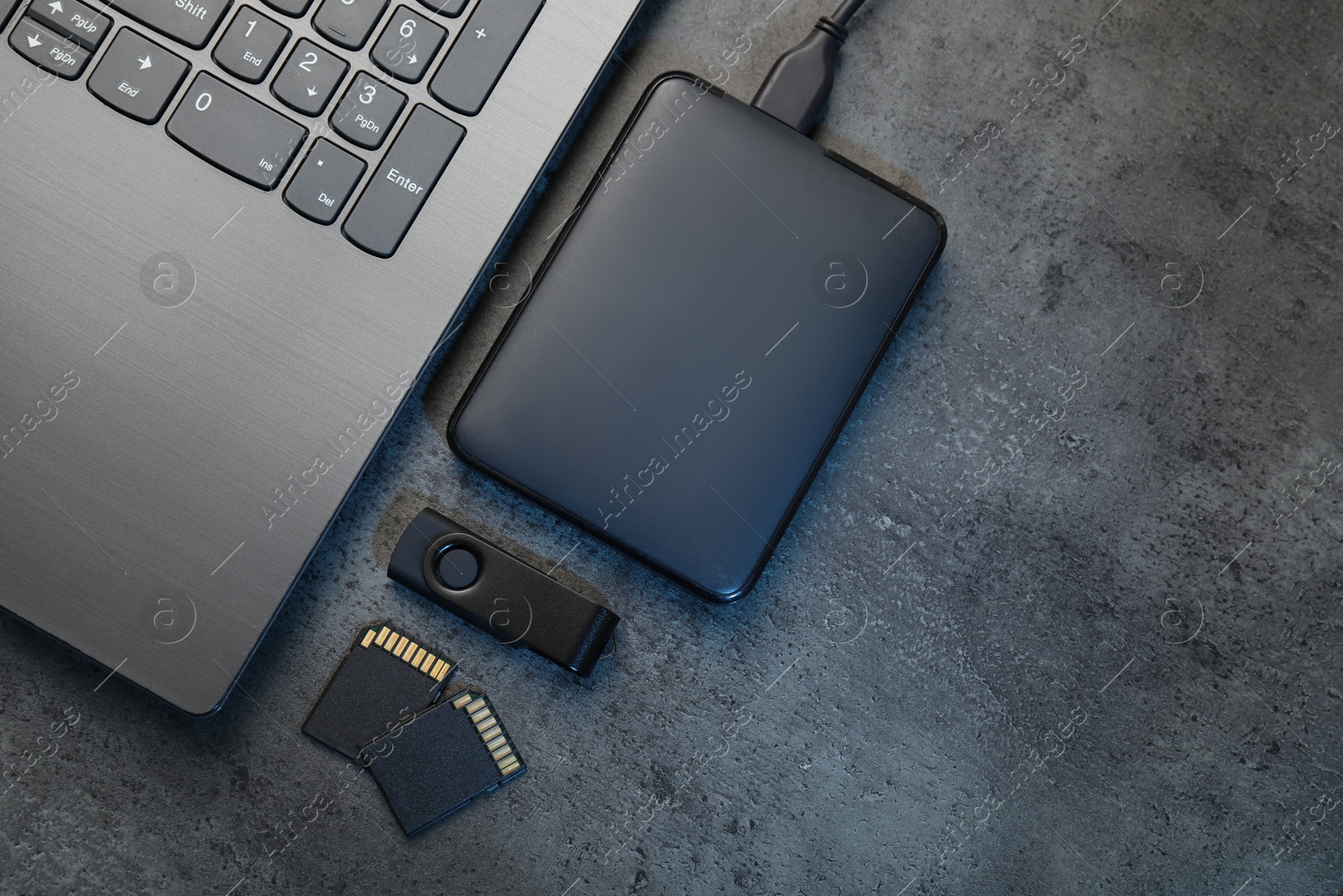 SD memory cards, USB flash drive, hard disk drive with cable and laptop on dark grey table, flat lay. Space for text Photo of SD memory cards, USB flash drive, hard disk drive with cable and laptop on dark grey table, flat lay. Space for text