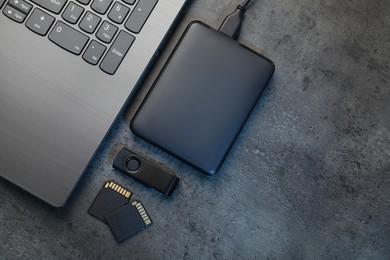 Photo of SD memory cards, USB flash drive, hard disk drive with cable and laptop on dark grey table, flat lay. Space for text