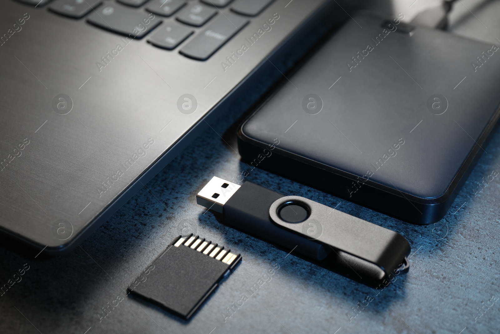 SD memory card, USB flash drive, hard disk drive and laptop on dark grey table, closeup Photo of SD memory card, USB flash drive, hard disk drive and laptop on dark grey table, closeup