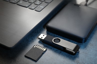 Photo of SD memory card, USB flash drive, hard disk drive and laptop on dark grey table, closeup