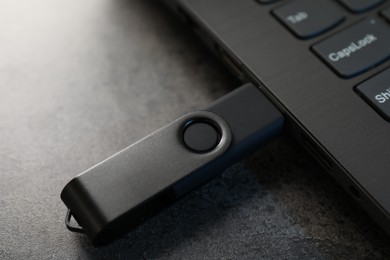 Photo of USB flash drive connected to laptop on dark grey table, closeup